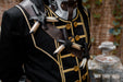 A close-up of a black military-style costume jacket with gold trim, brown shoulder straps, and multiple bone-like decorative accents, shown on a mannequin or dress form against an outdoor blurred background.