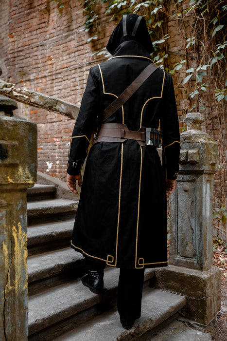A person viewed from behind wearing a long black hooded robe with gold trim and brown belt details, walking up outdoor stone stairs against a brick wall and vines.